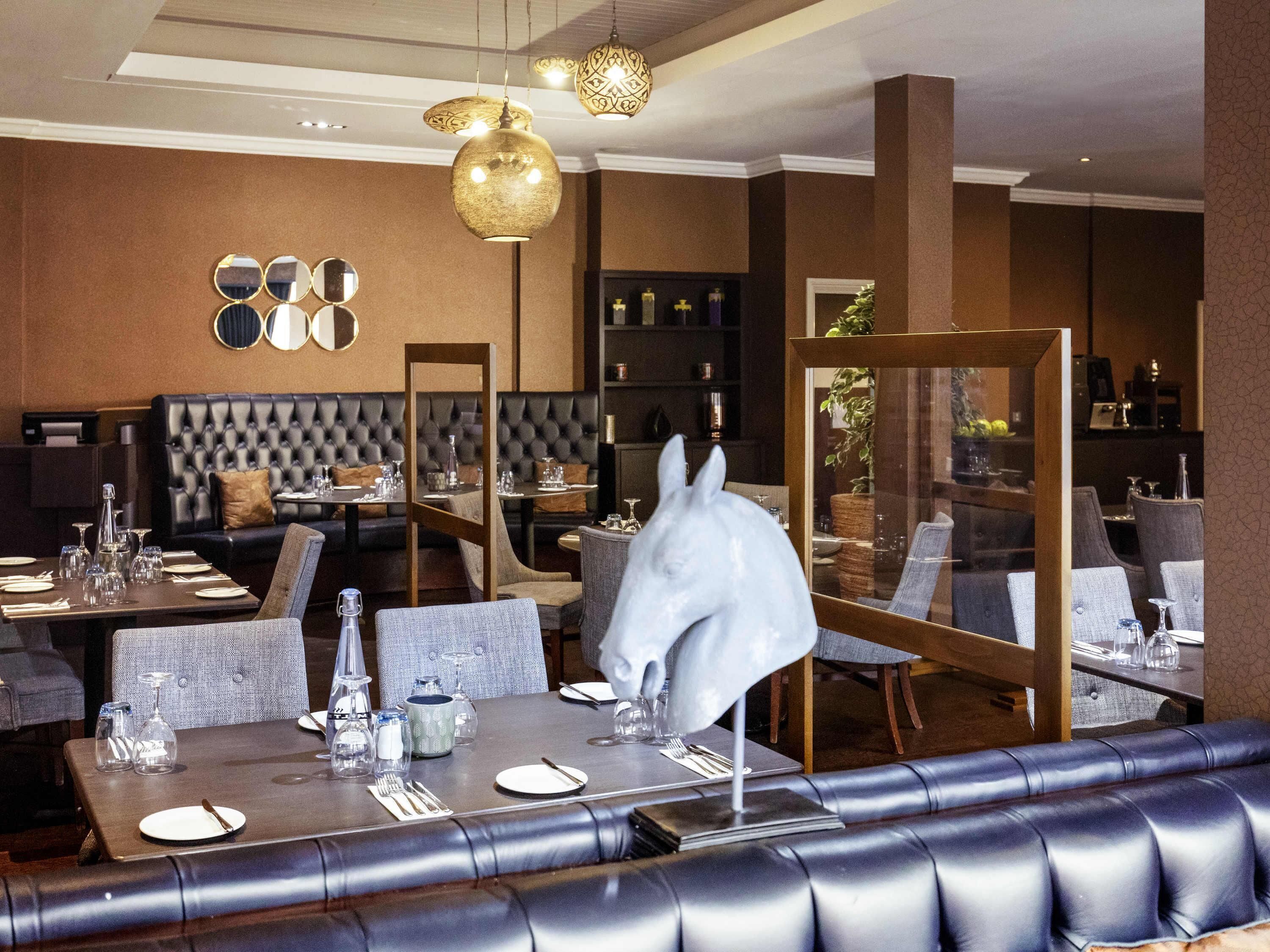 A restaurant with leather booths, round tables, and hanging pendant lights.