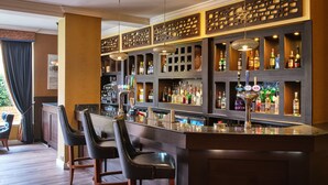 A bar area with a dark wood bar counter, two black leather bar stools, and a variety of liquor bottles. - Mercure Milton Keynes (Milton Keynes)