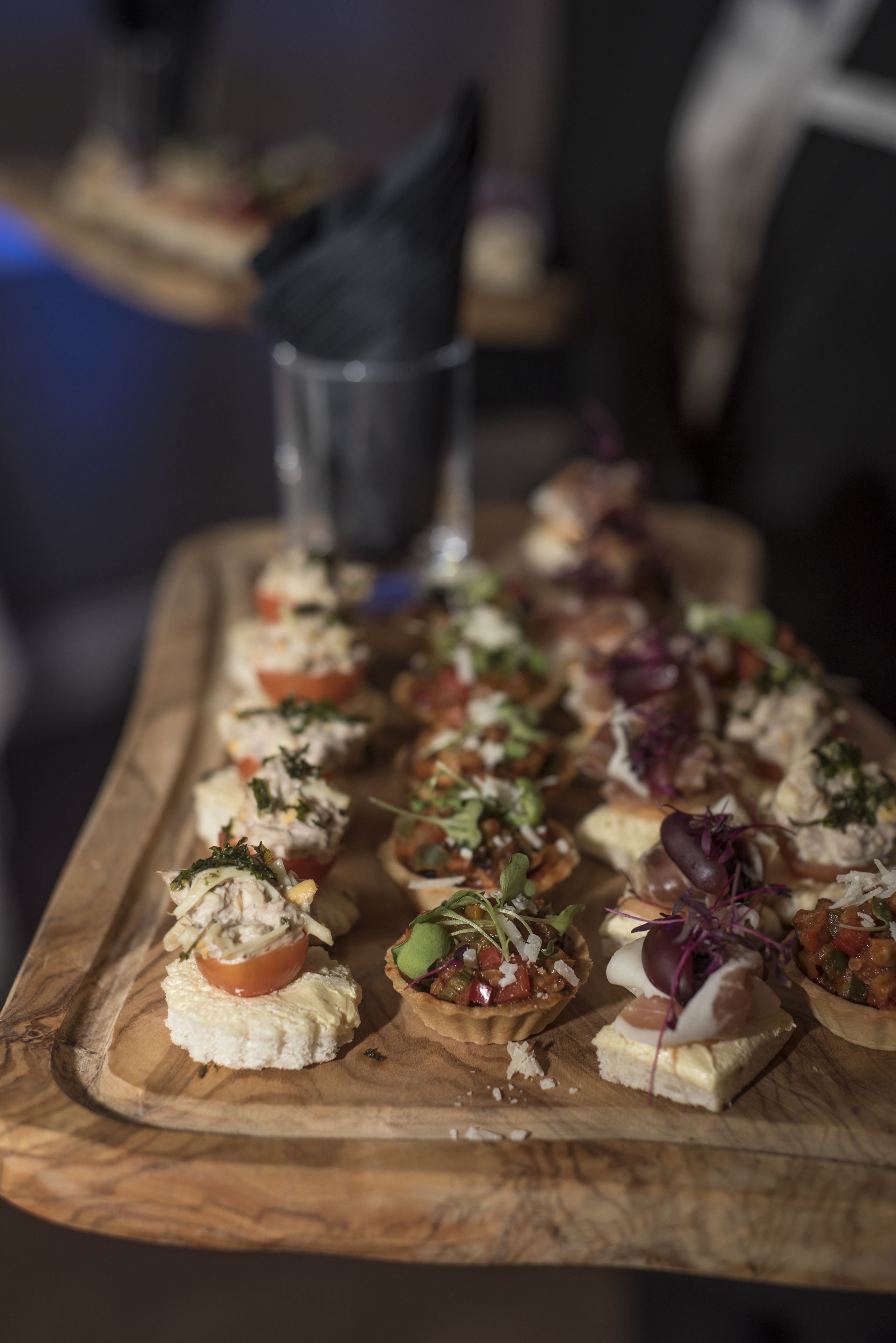 En træserveringsbakke med forskellige appetizers, herunder fyldte tomater og minitærter, på et bord.