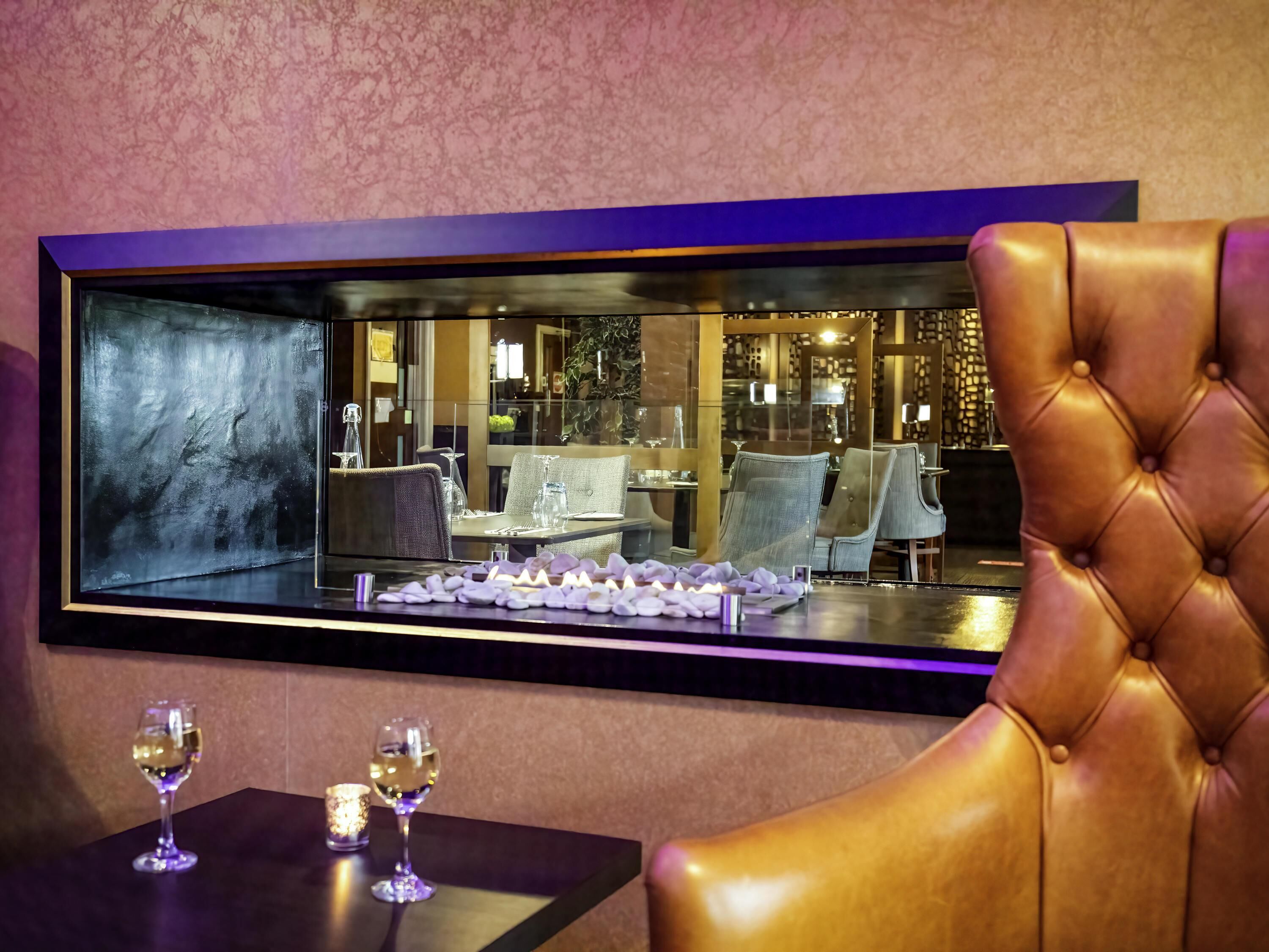 A dining area with a glass partition, leather chairs, and a table with wine glasses and a candle.