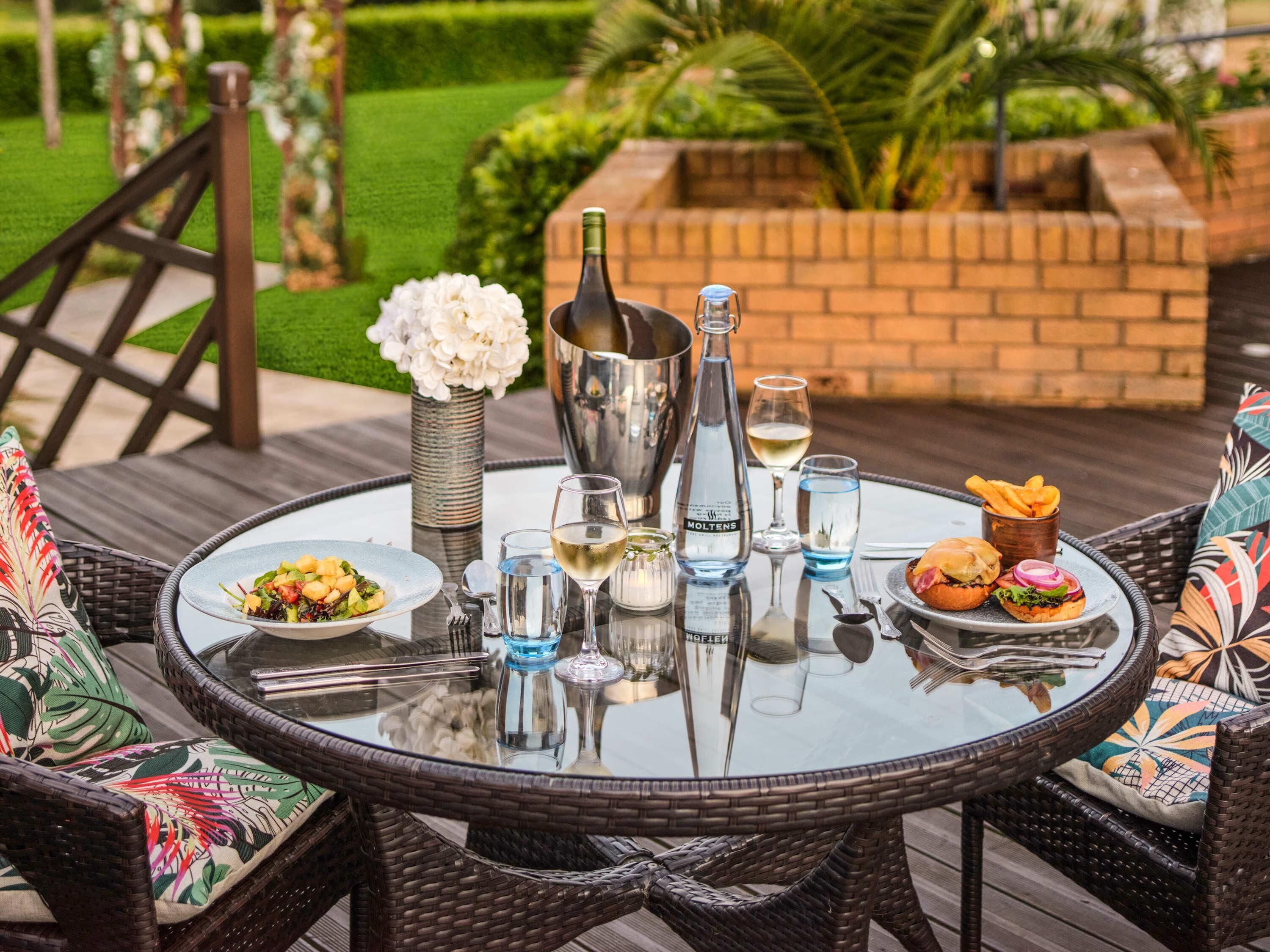 A round glass table with a bottle of Moltens, two glasses of white wine, a plate of food, and a basket of fries.