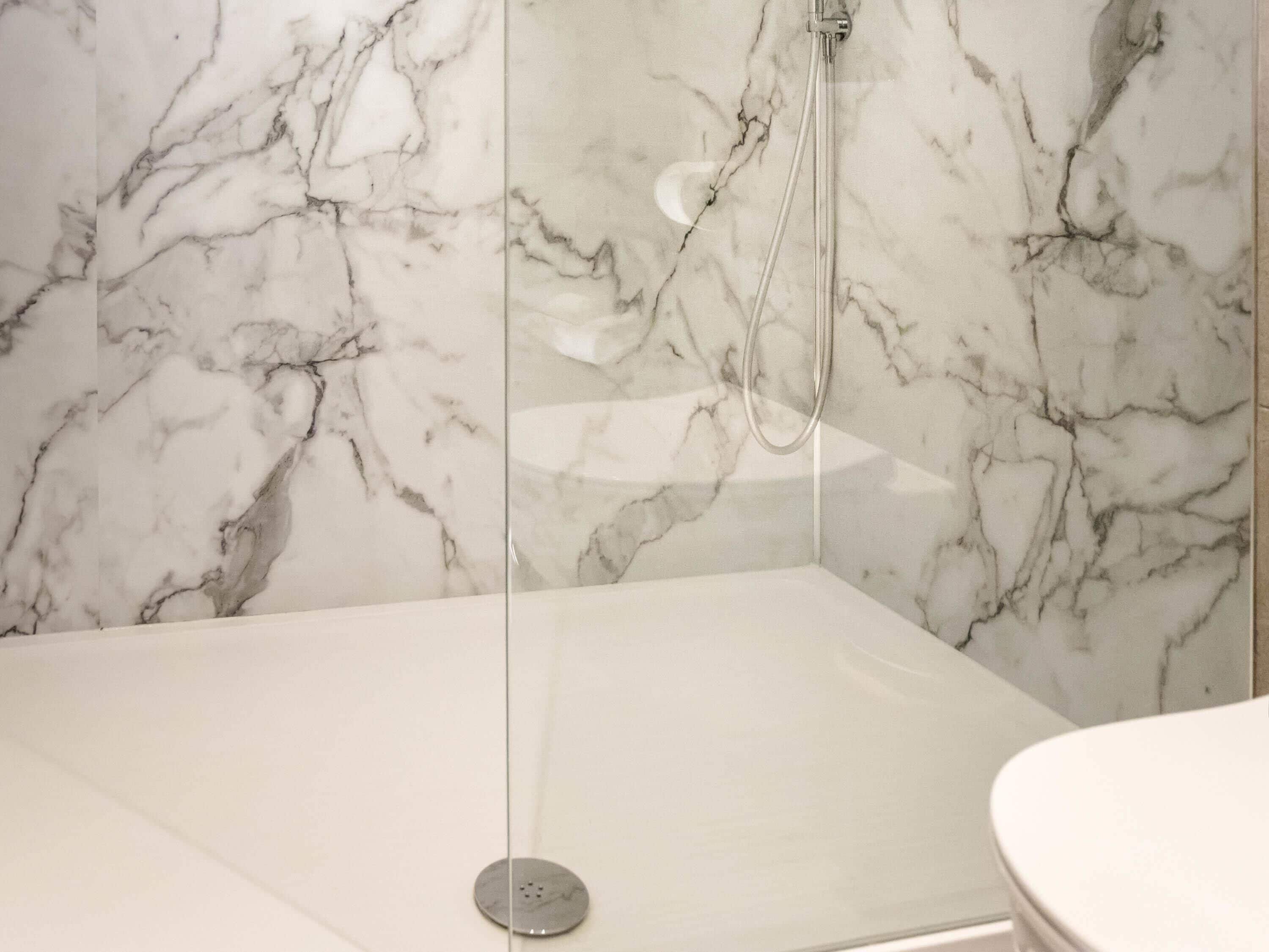 Un baño moderno con pared de ducha de mármol y un área separada para el inodoro.
