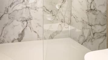 Un baño moderno con pared de ducha de mármol y un área separada para el inodoro.