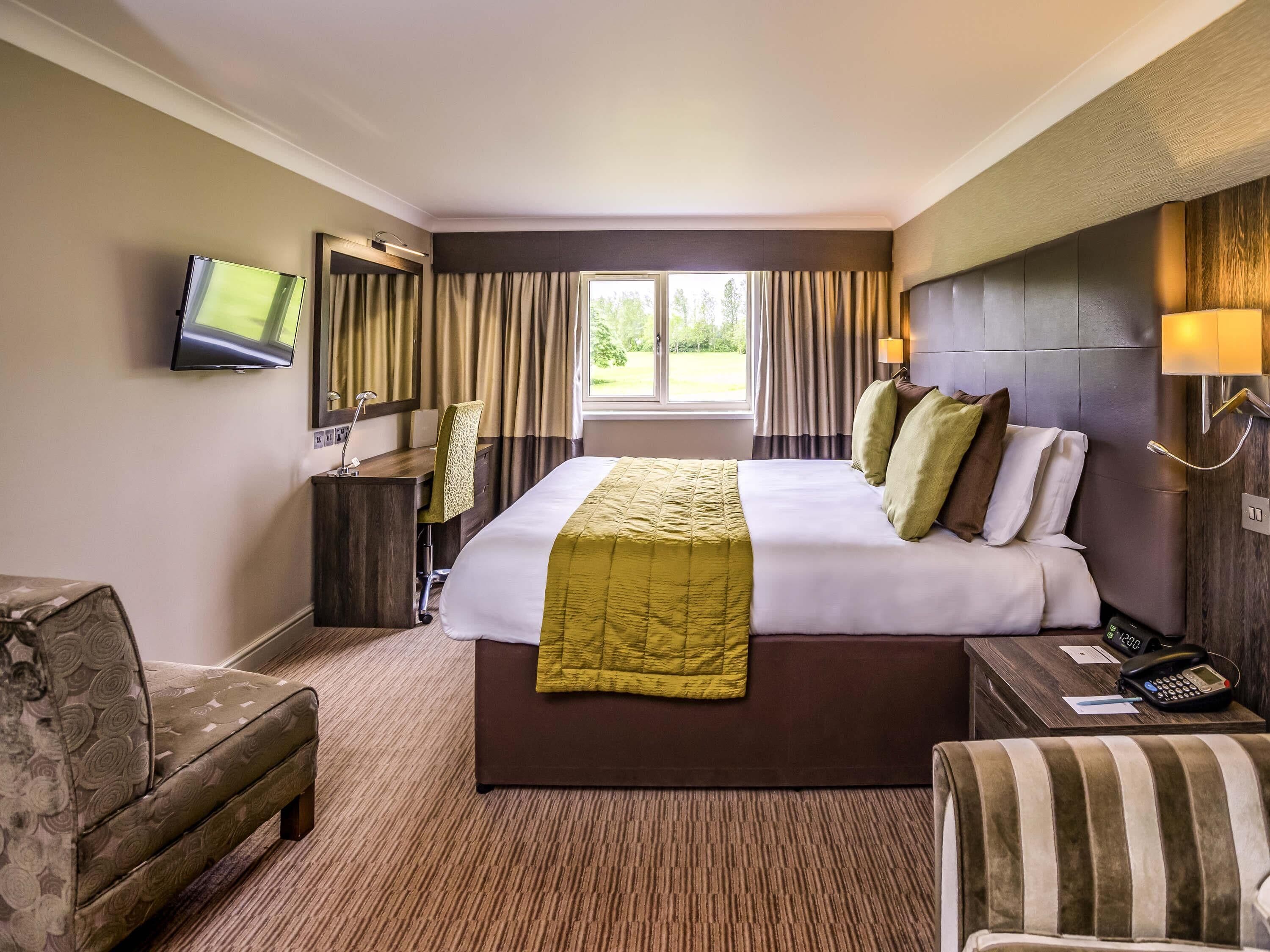 A hotel room with a bed, a desk, a chair, a television, and a window with curtains.