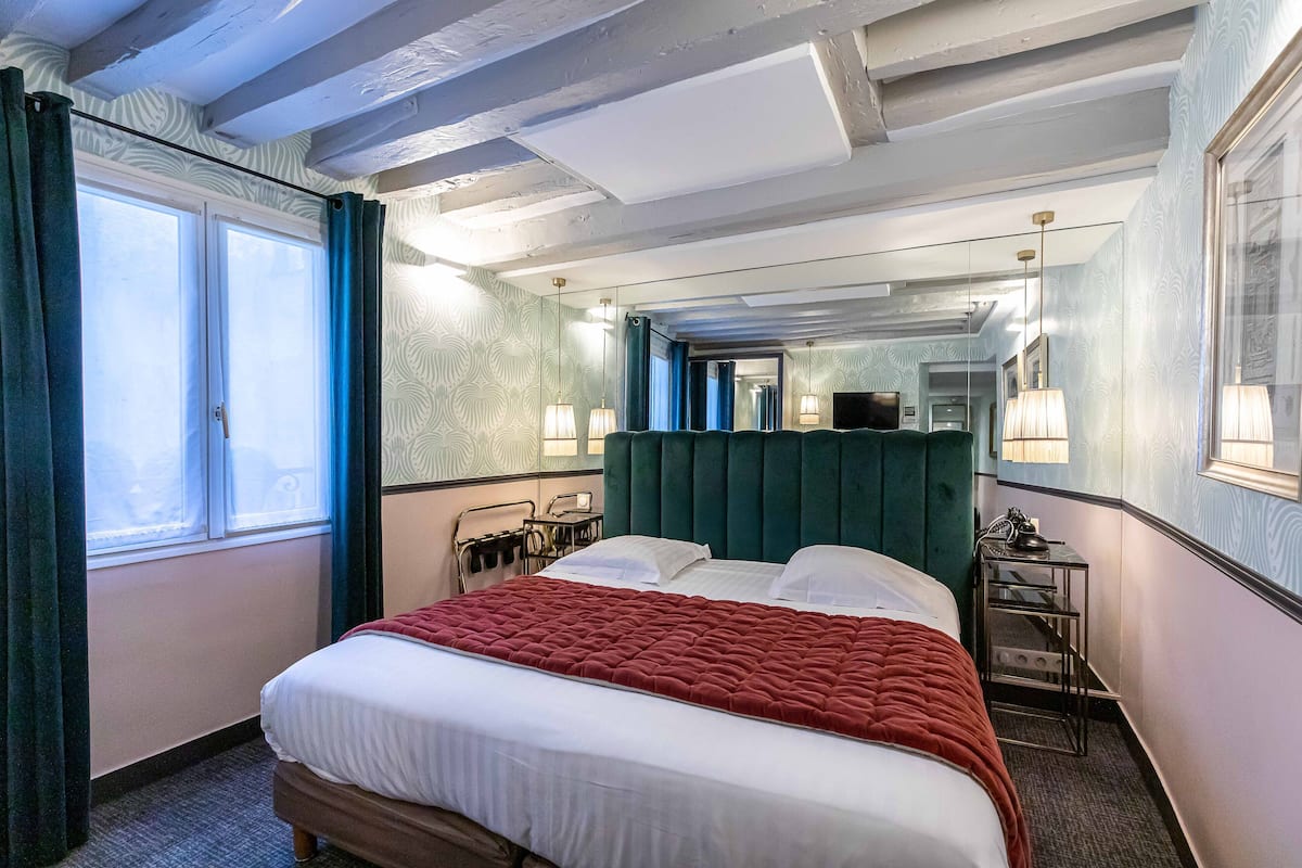 A hotel room with a large bed, a mirror, a bedside table, and a window with curtains.