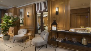 A lobby with wooden paneling, two upholstered armchairs, a small round table, a potted plant, and a display shelf with decorative items.