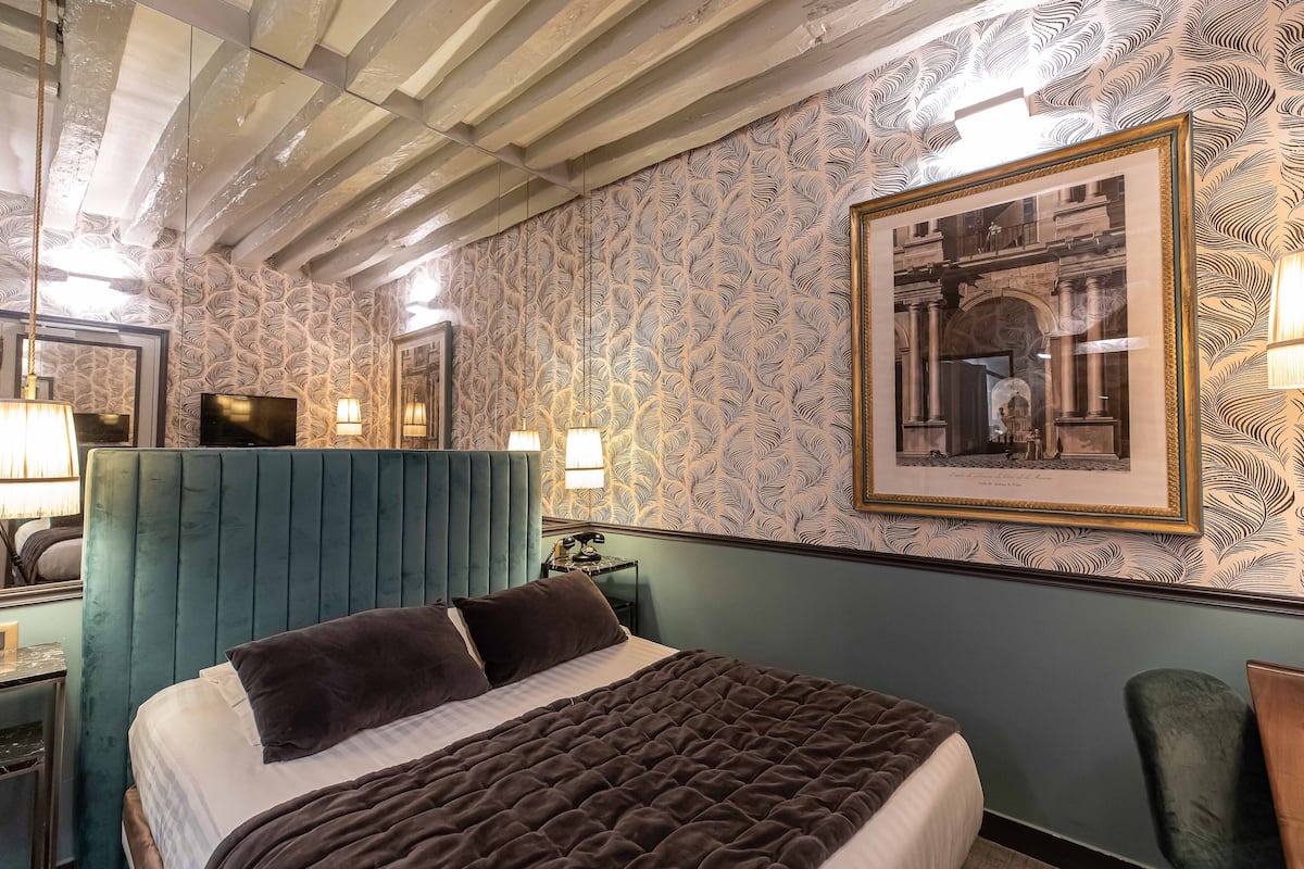 A hotel room with a large bed, a blue headboard, a patterned wallpaper, and a framed picture on the wall.