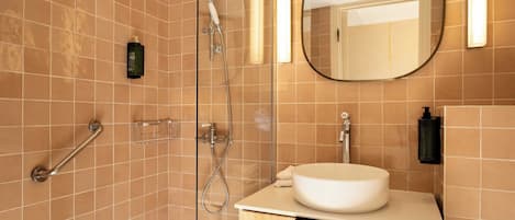 A bathroom with a glass shower enclosure, a round mirror, a sink with a countertop, and a towel rack.