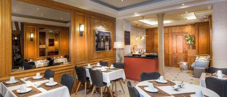 A hotel lobby with multiple dining tables, a reception desk, and a bar area.