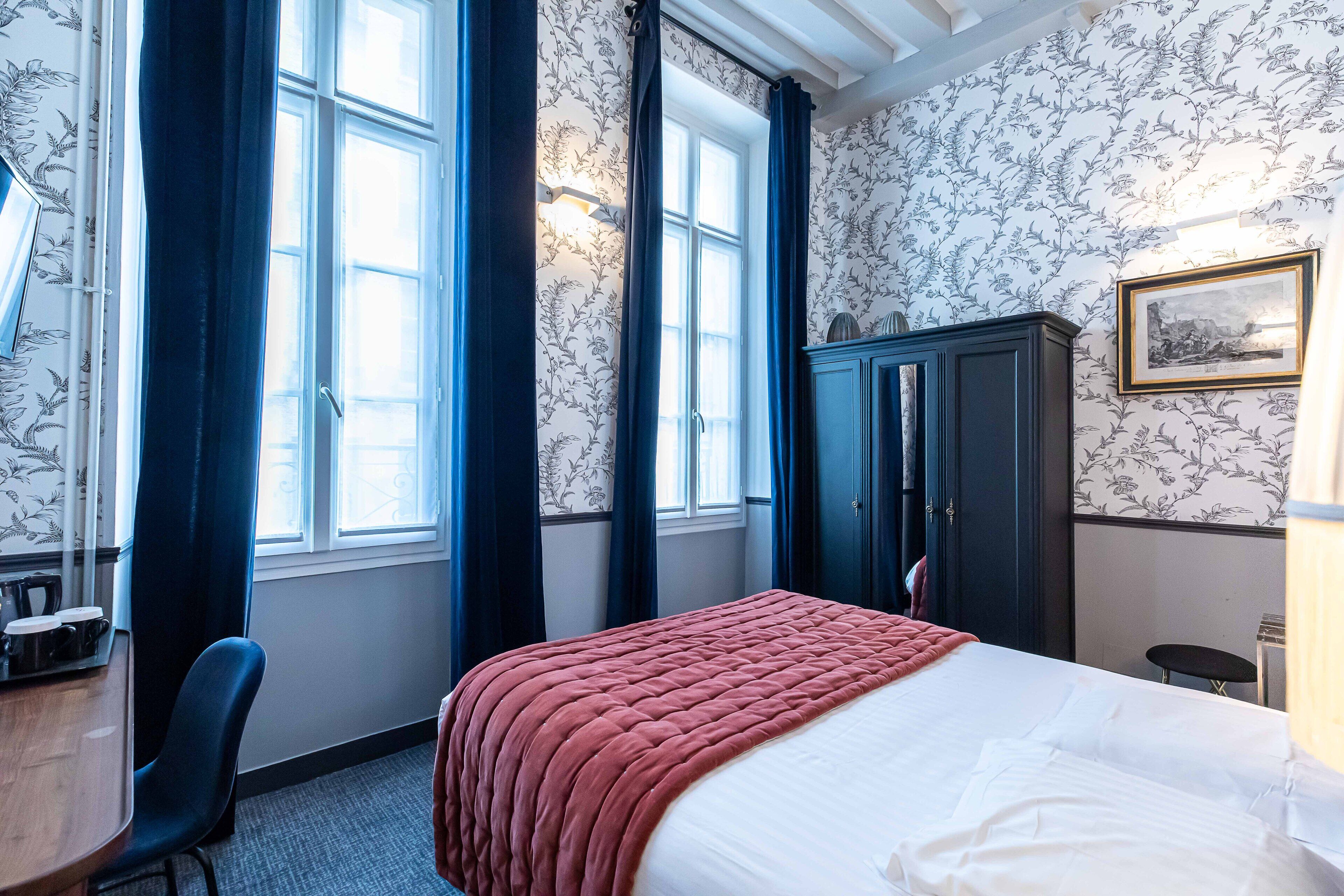 A hotel room with a bed, a desk, a chair, a wardrobe, and a window with curtains.