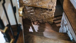 A wooden staircase with a stone wall and metal railing.