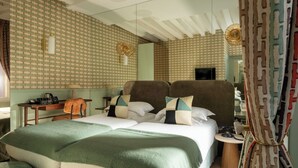 A hotel room with a large bed, a desk with a chair, a small table, and a television.