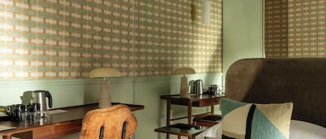 A hotel room with a brick-patterned wall, a wooden desk with a chair, a bed with a pillow, and a hanging light fixture.