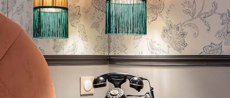 A bedroom with a bed, a nightstand with a telephone, and two hanging lamps.