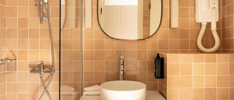 A bathroom with a round mirror, a sink, a handheld showerhead, and a towel rack.