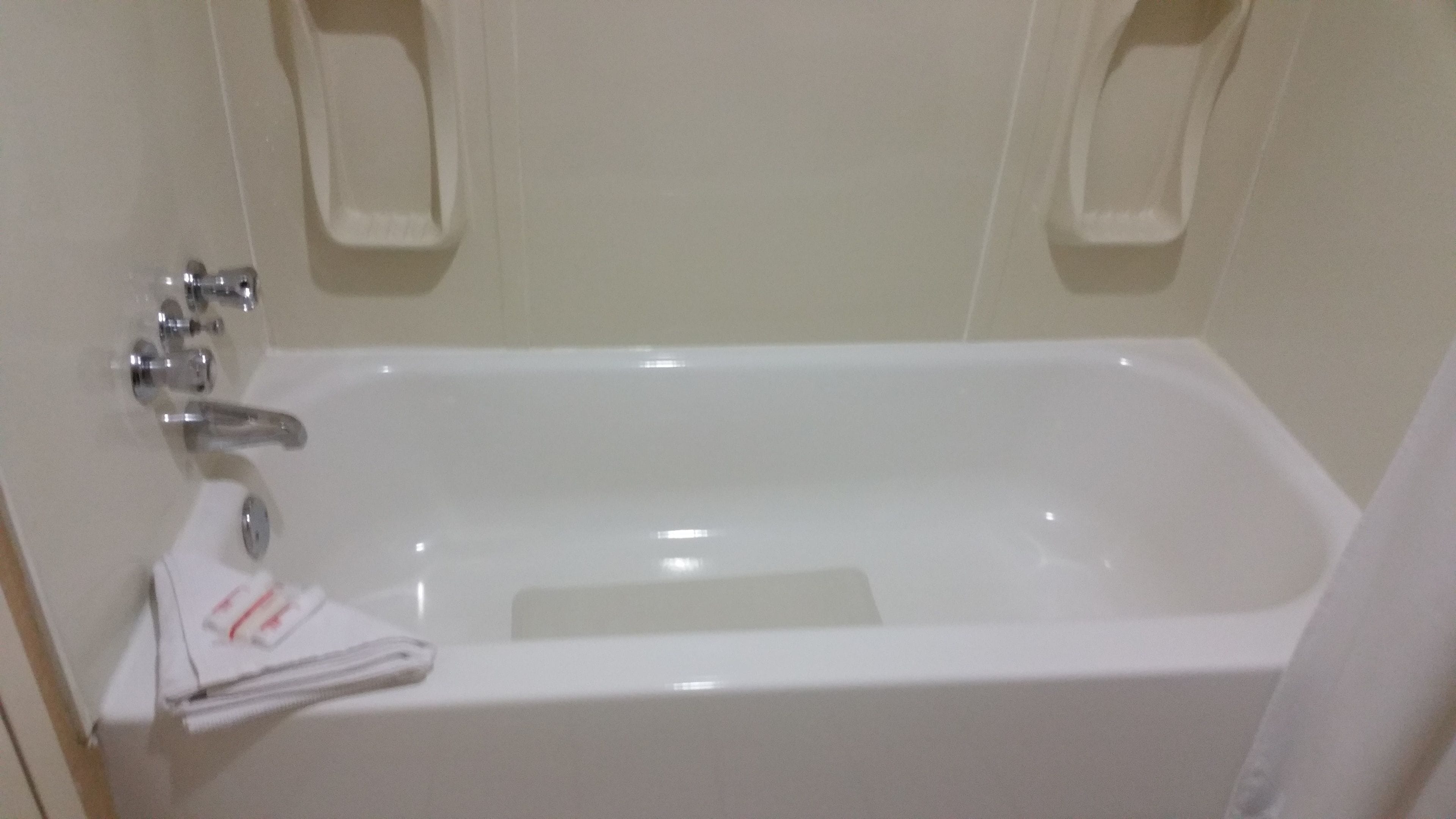A white bathtub with a single faucet and a small shelf above it.