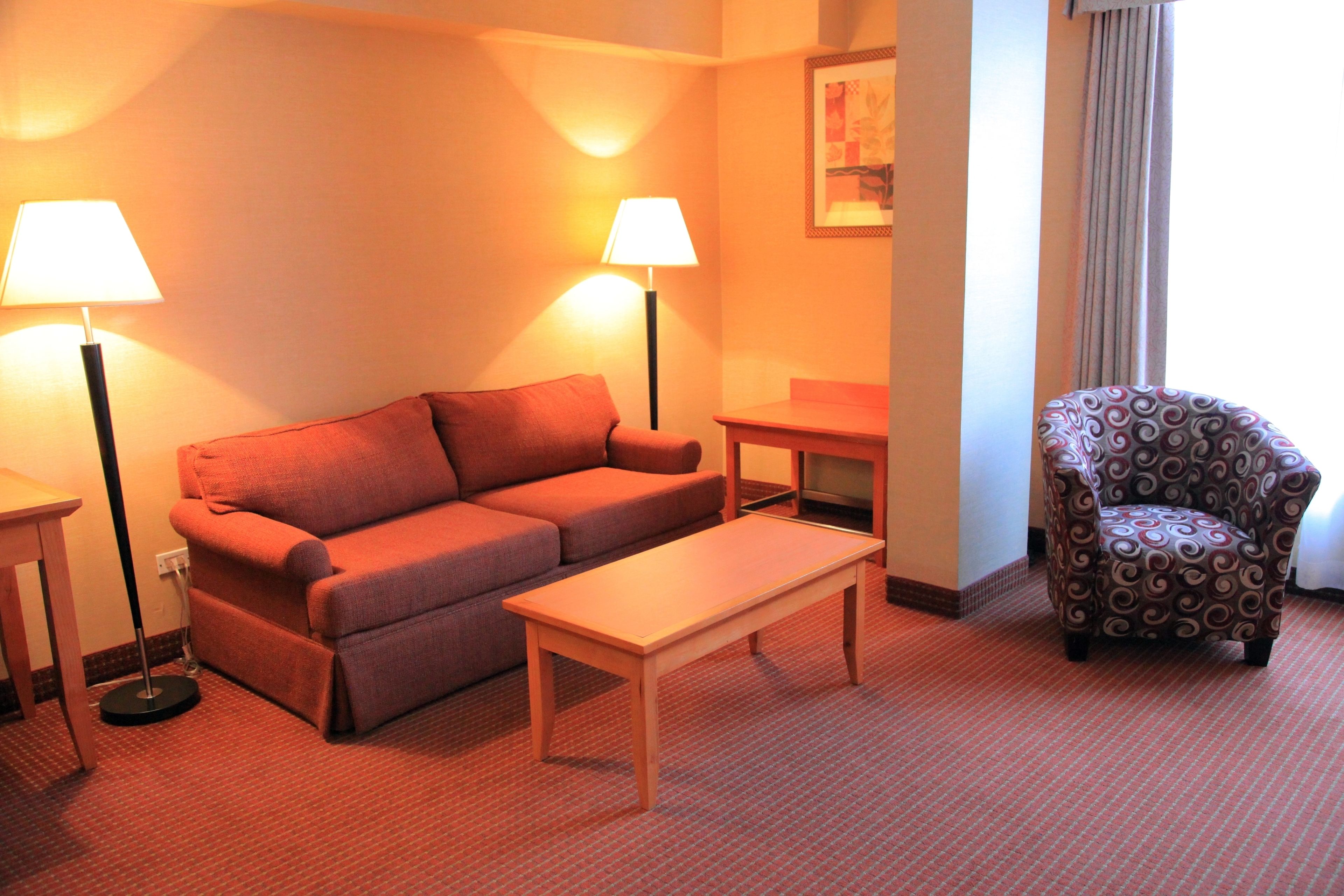 Habitación de hotel con sofá, una mesita, un sillón estampado y dos lámparas.