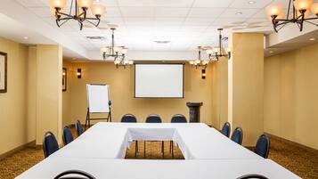 A conference room with a long table, chairs, a projector screen, and chandeliers.