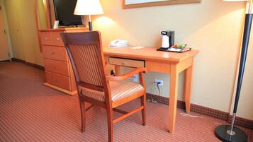 A hotel room with a wooden desk, a chair, a television, a lamp, and a coffee maker.
