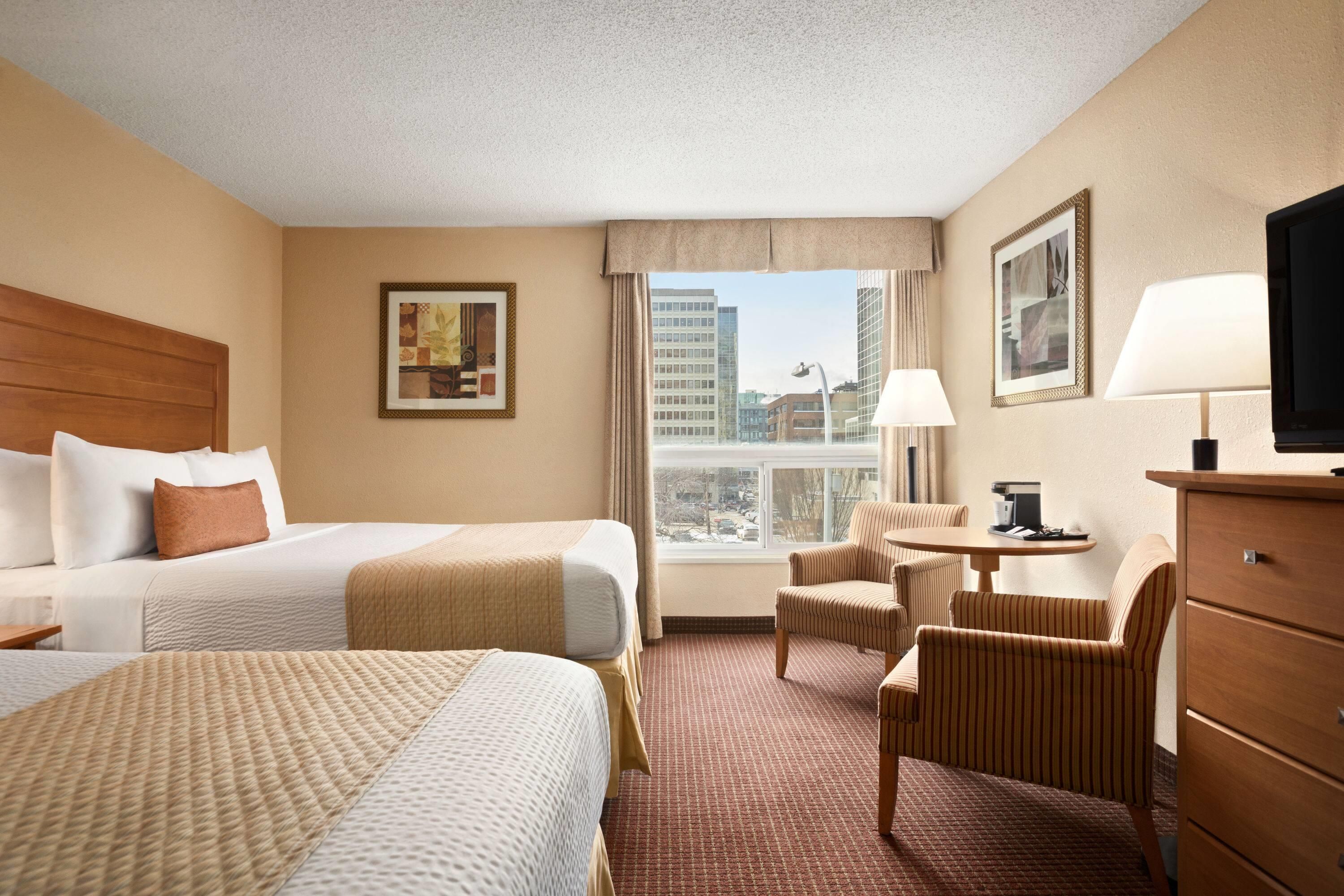 Habitación de hotel con dos camas, un escritorio con lámpara, una silla y televisión.