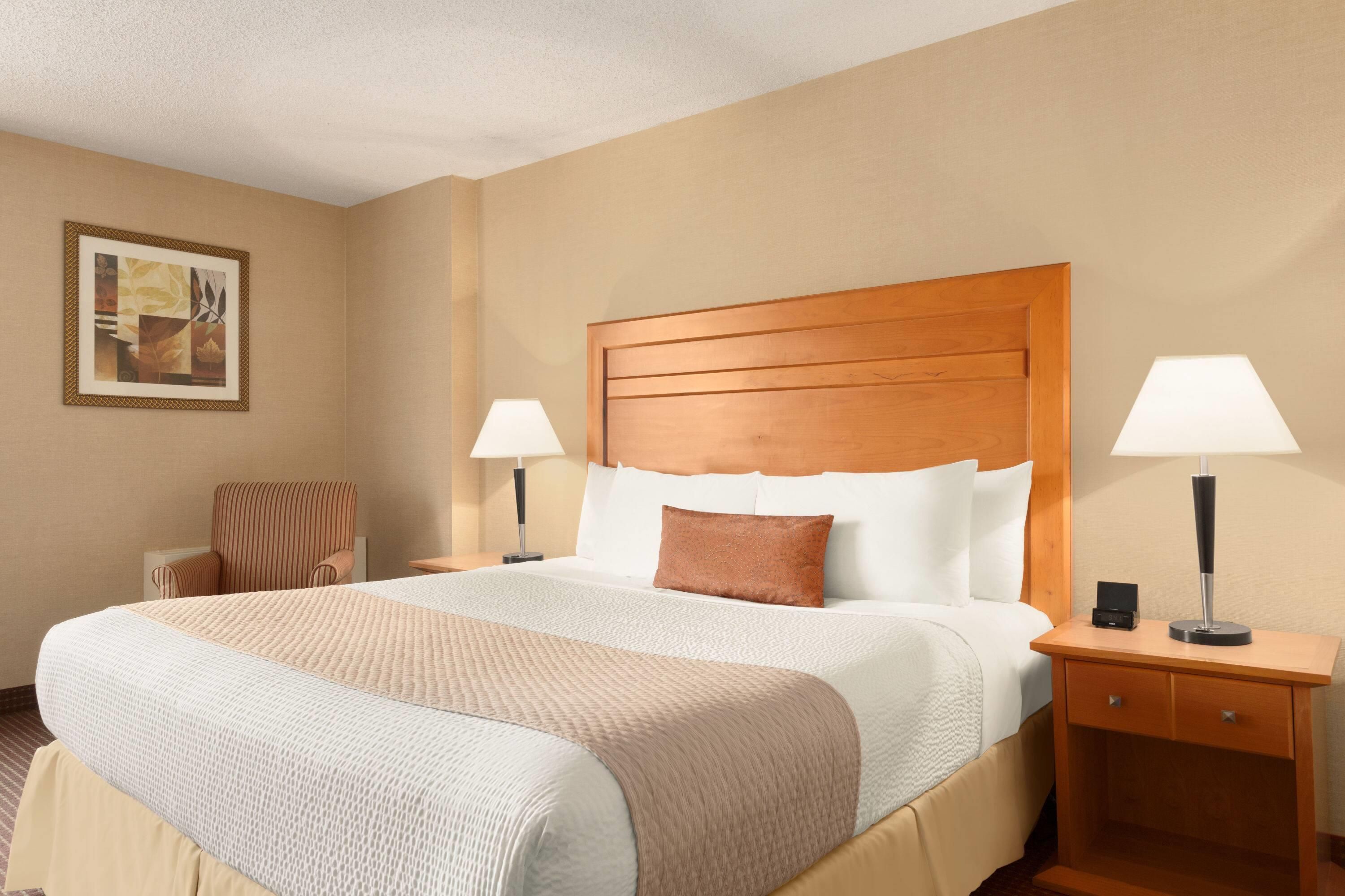 Quarto de hotel com uma cama grande, duas mesas de cabeceira, uma cadeira e um quadro na parede.