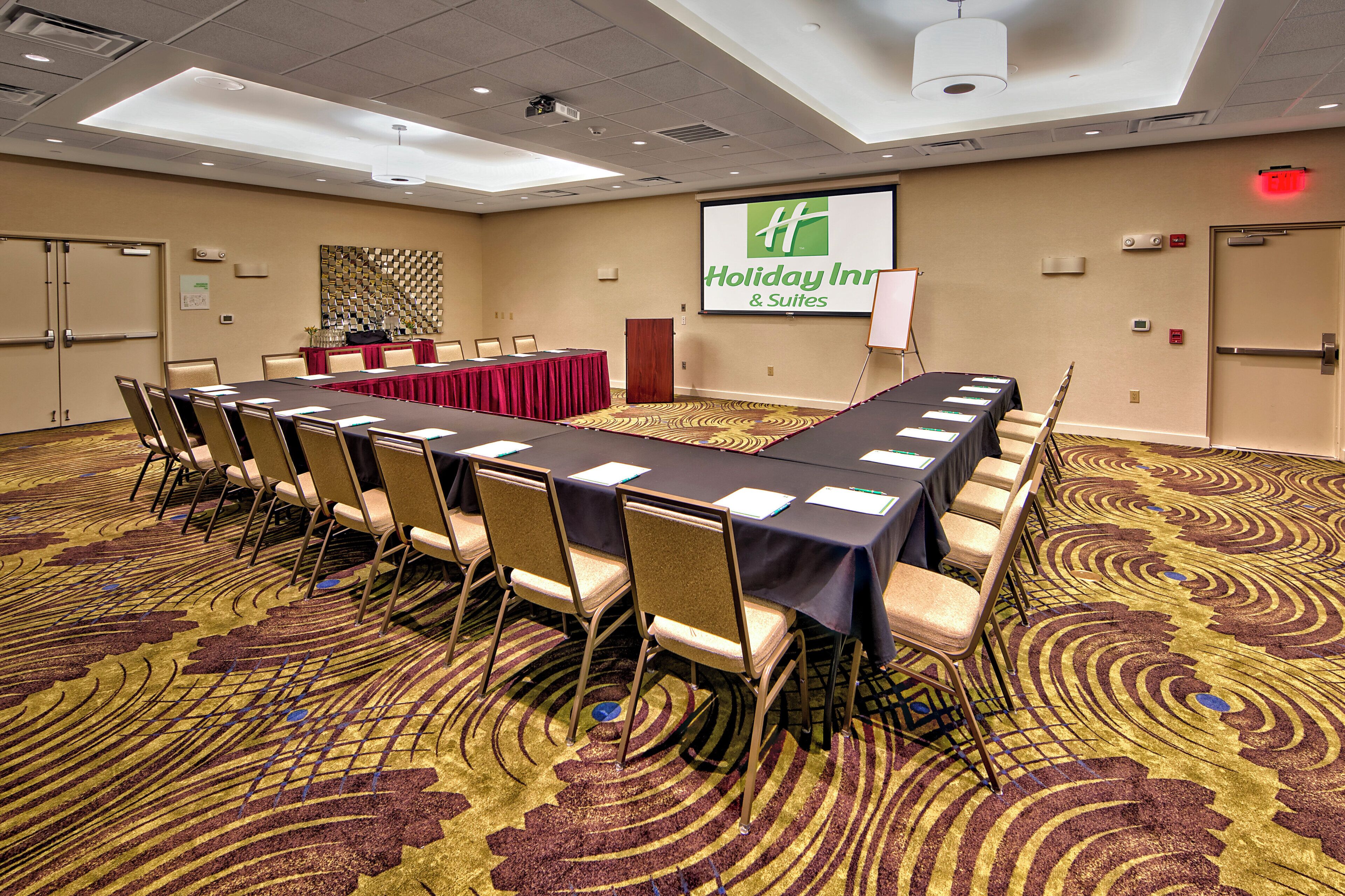 A conference room with a long table, chairs, and a screen displaying the Holiday Inn & Suites logo.