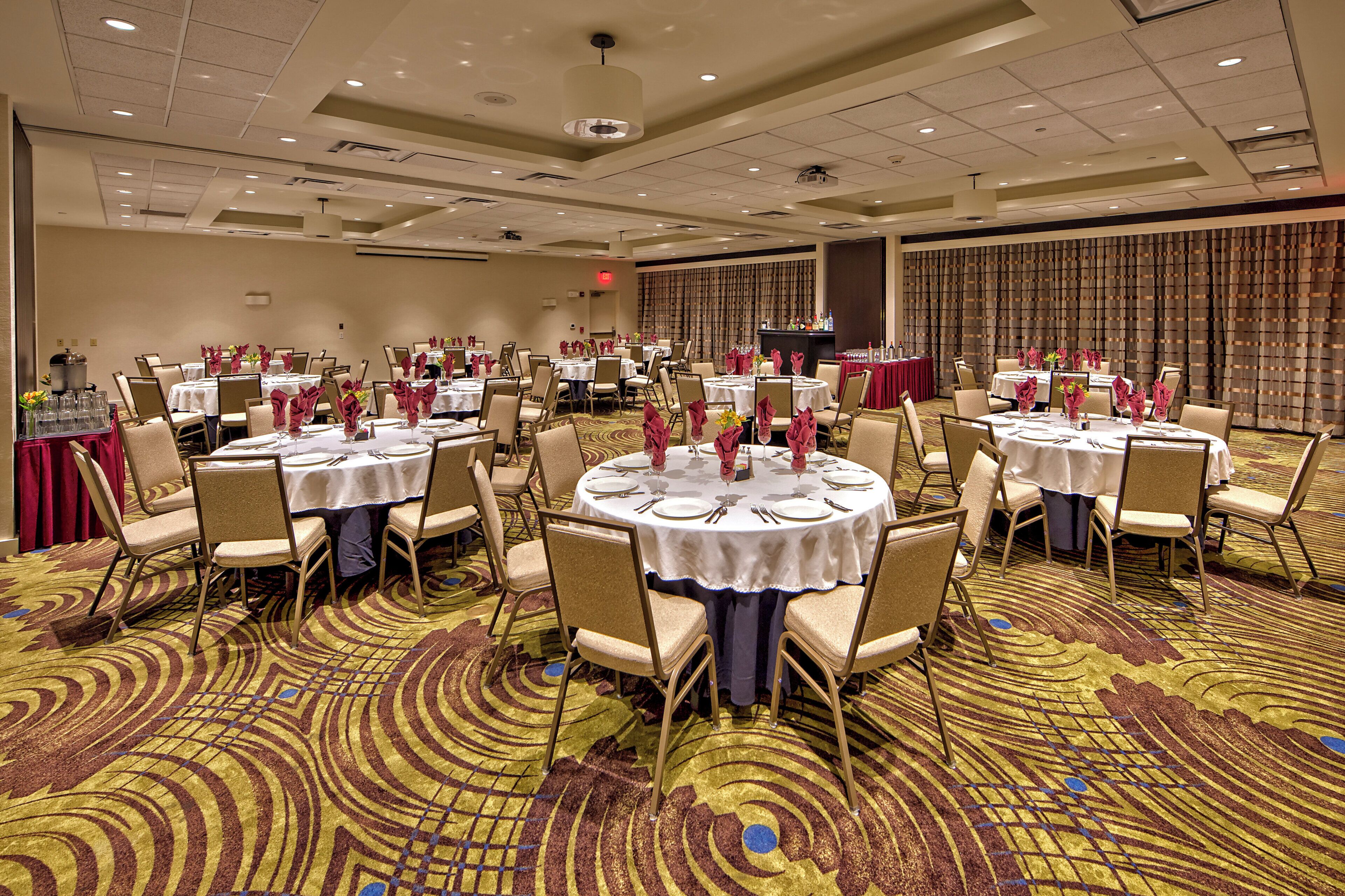 Une salle de banquet avec des tables rondes, des chaises et un sol recouvert de moquette.