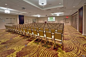 A conference room with rows of chairs, a projection screen, and a carpeted floor. - Holiday Inn Hotel & Suites Tupelo North by IHG (Tupelo)