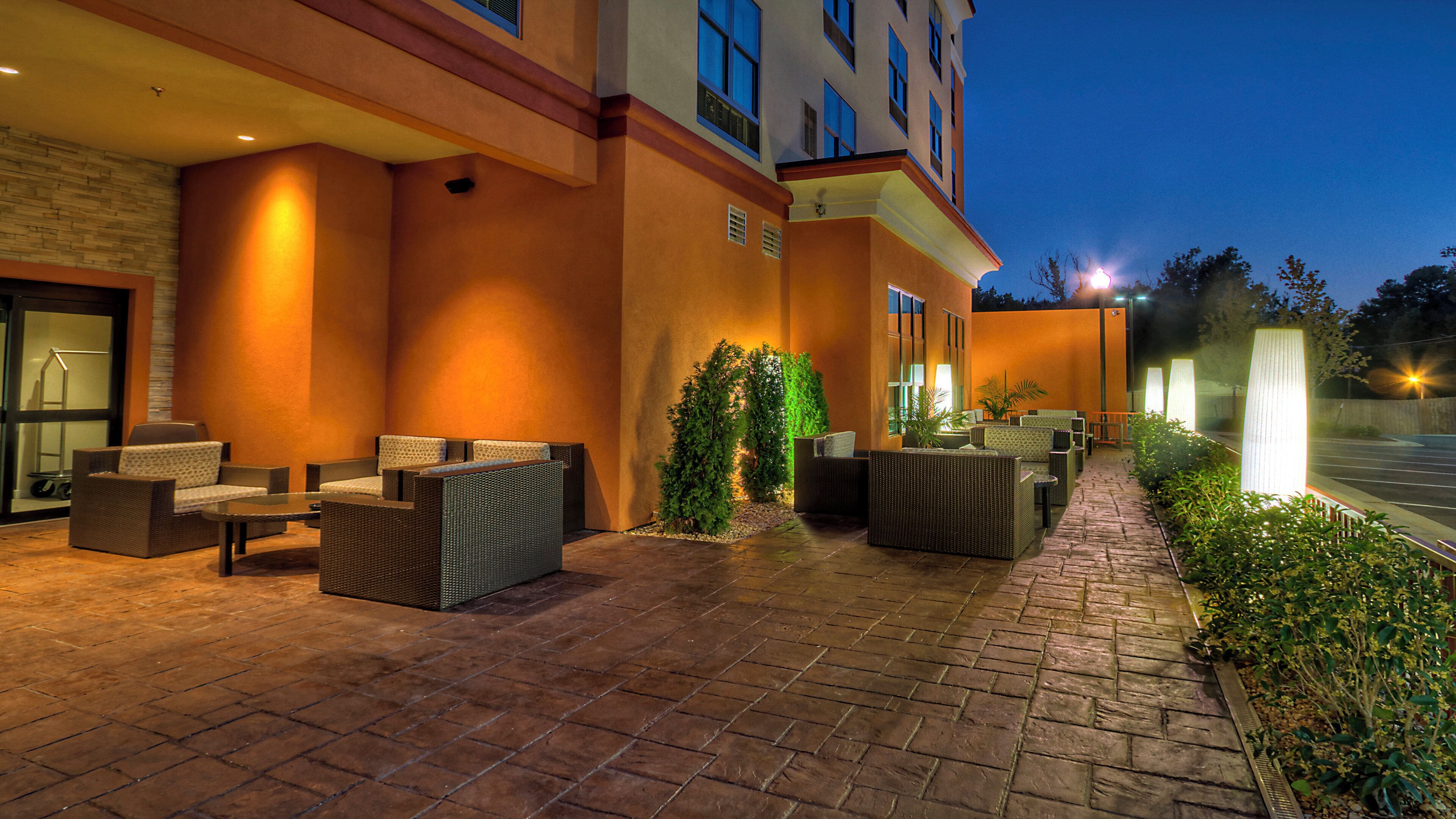 An outdoor seating area with wicker furniture and planters, a paved walkway, and a building with large windows.