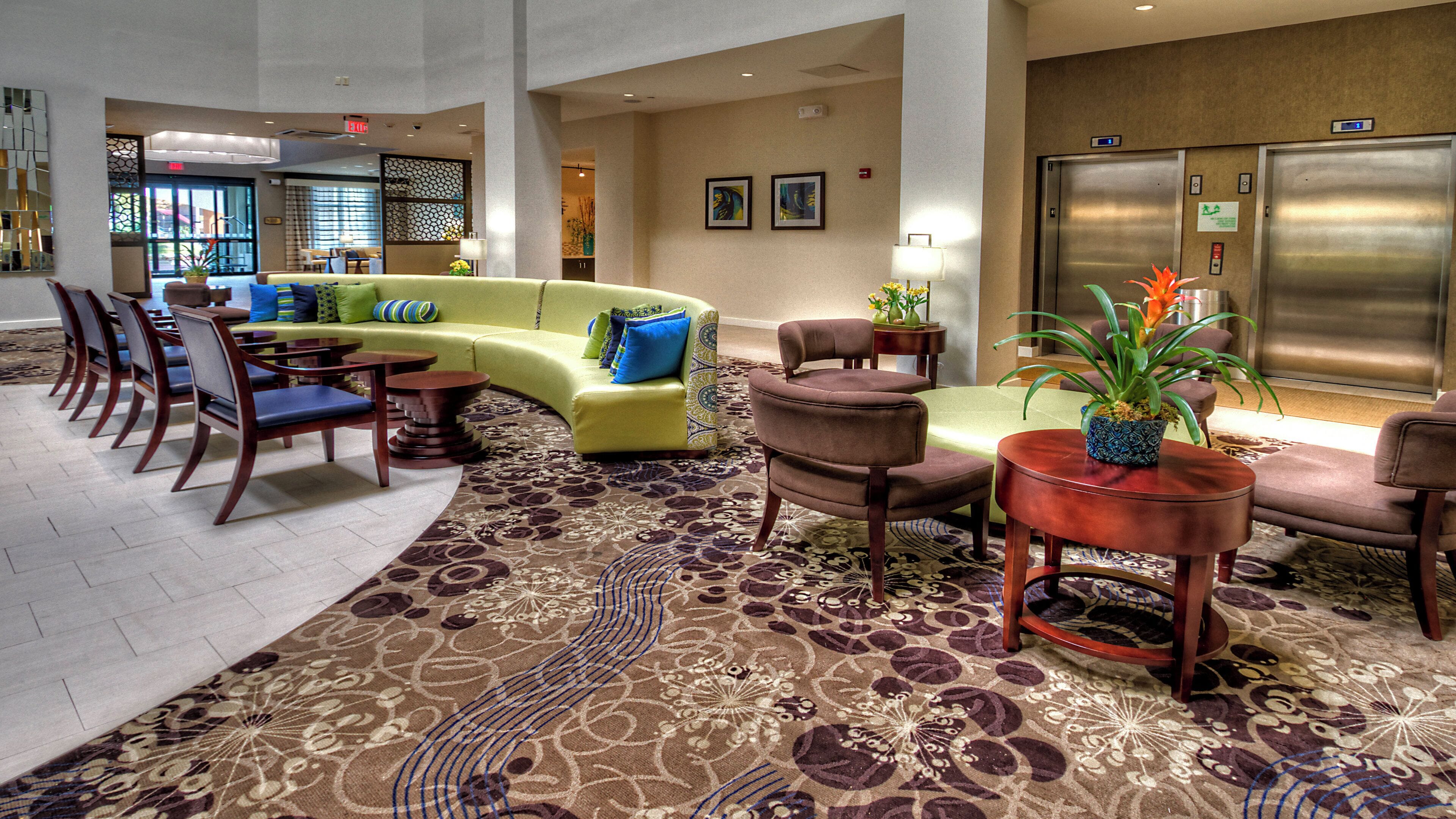 A lobby with a curved sofa, multiple chairs, a patterned carpet, and an elevator.