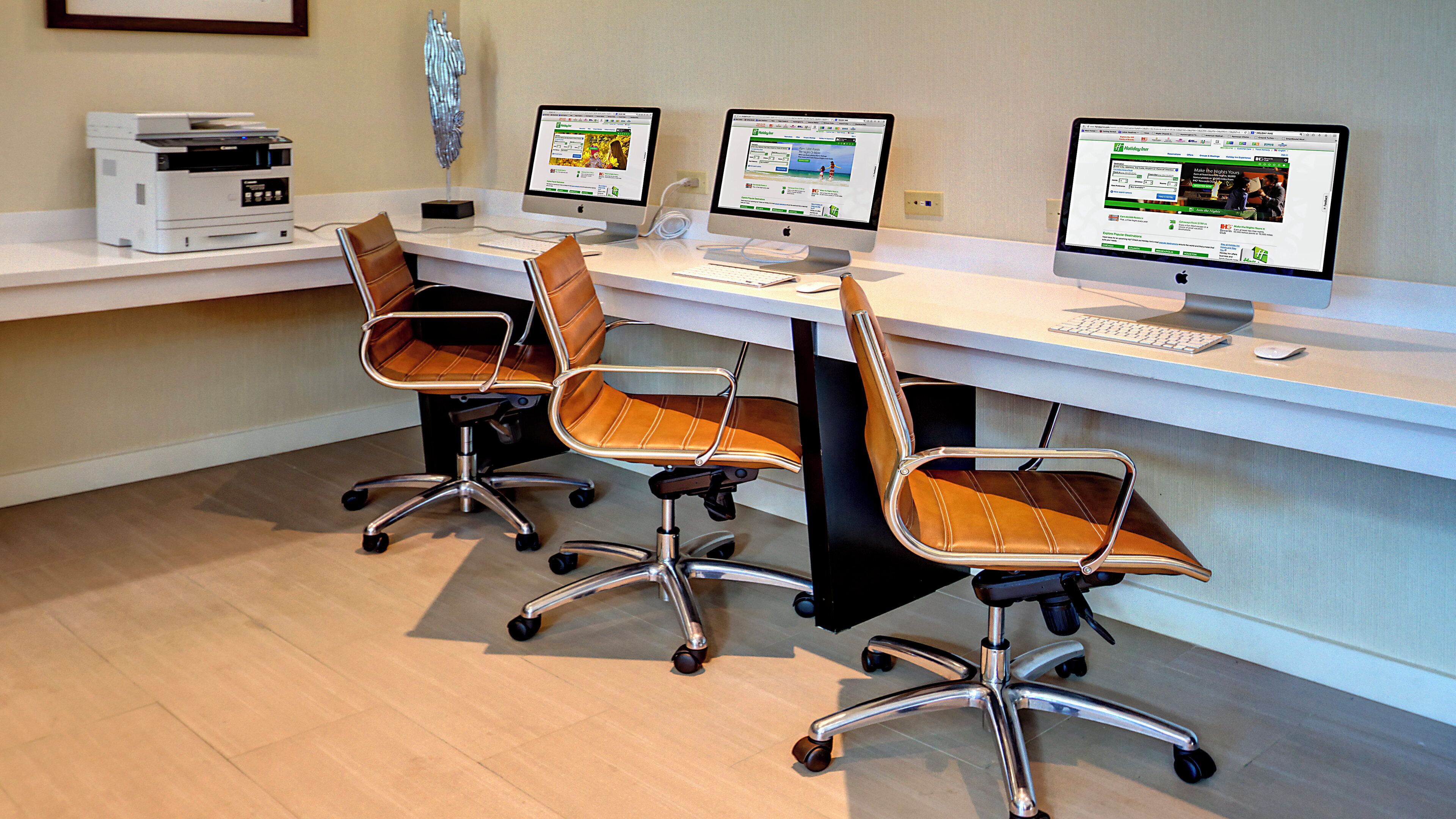 Un espace de travail comprenant trois bureaux, chacun équipé d’un écran d’ordinateur, d’un clavier et d’une souris. On y trouve également trois chaises de bureau à roulettes. Une imprimante est visible sur le côté gauche de l’image.