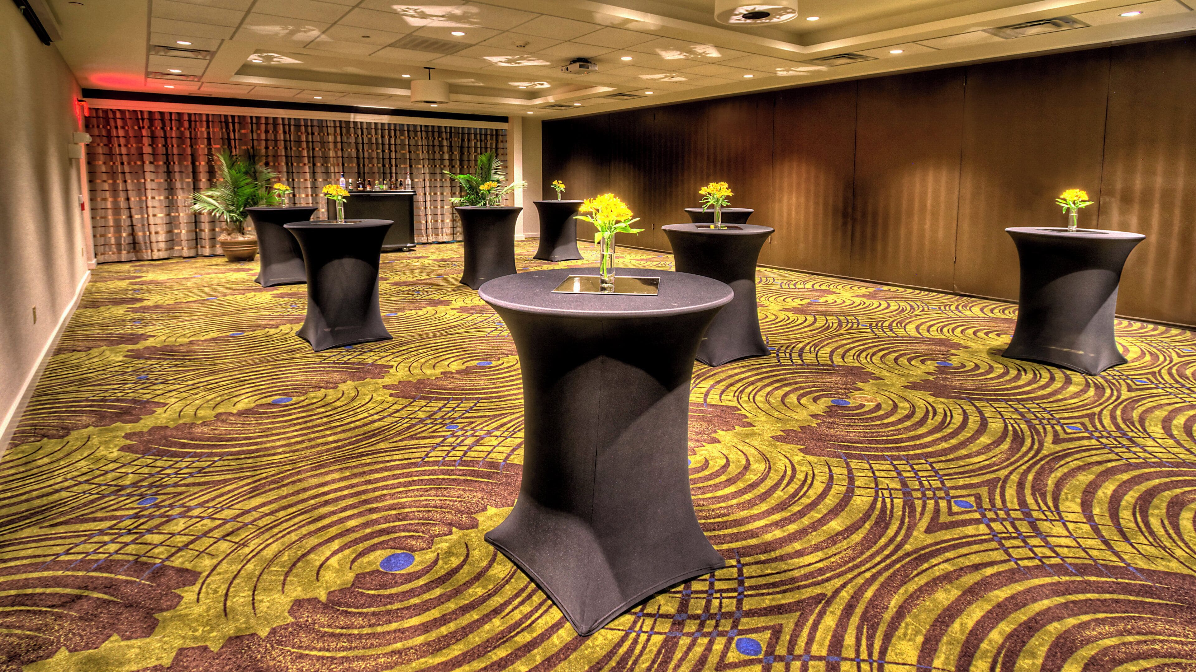 A carpeted room with round tables and potted plants.