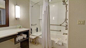 Un baño moderno con ducha de vidrio, tocador con espejo y repisa con toallas.