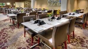 A hotel dining area with multiple tables set for guests, featuring a carpeted floor and modern decor. - Holiday Inn Hotel & Suites Tupelo North by IHG (Tupelo)