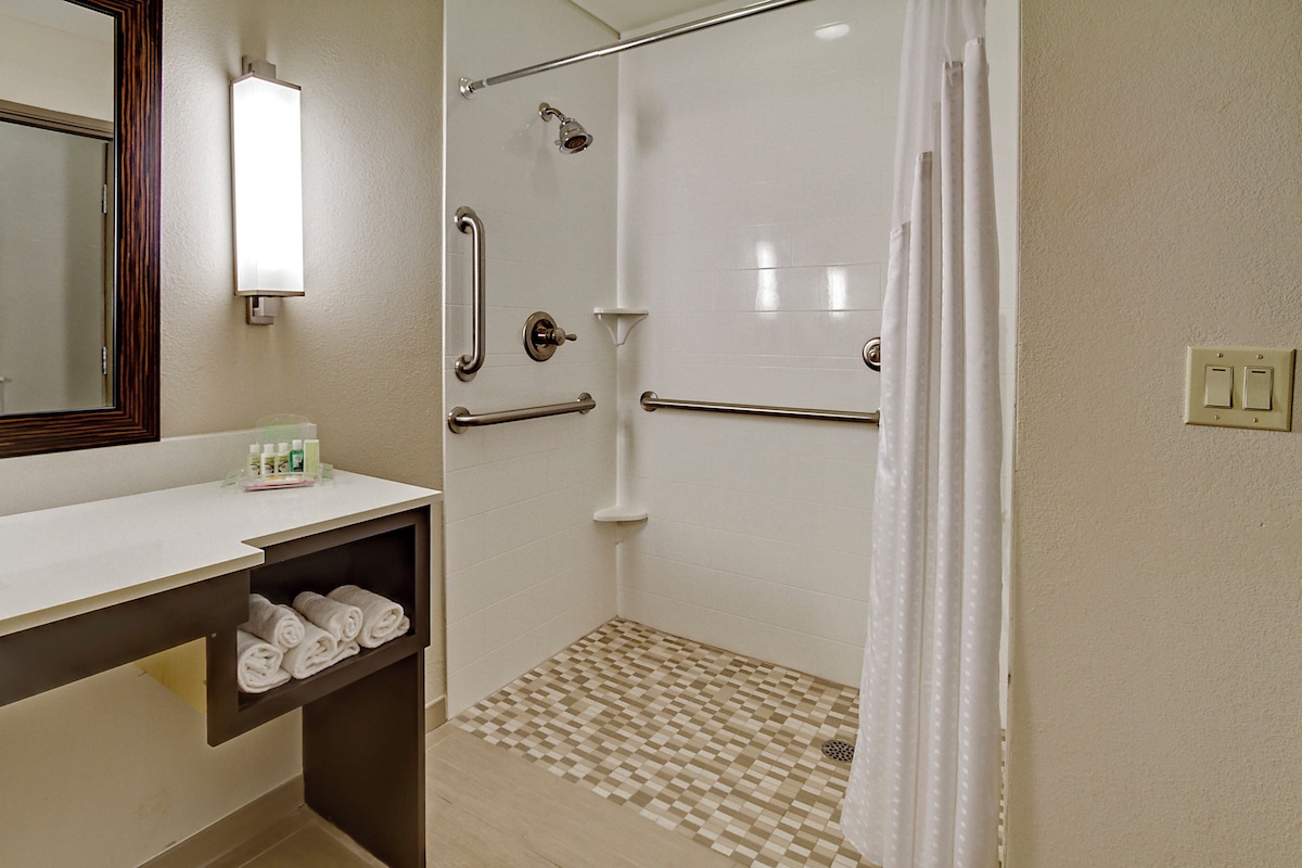A bathroom with a shower, a mirror, a towel rack, and a shelf with toiletries.