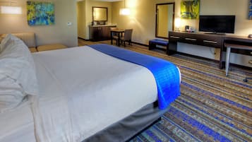 Ein Hotelzimmer mit einem großen Bett, einem Schreibtisch, einem Sessel, einem Fernseher und Bildern an den Wänden.