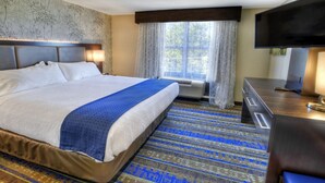 A hotel room with a large bed, a flat-screen TV, a desk, and a window with curtains. - Holiday Inn Hotel & Suites Tupelo North by IHG (Tupelo)