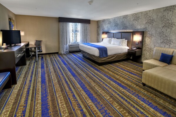 A hotel room with a large bed, a desk with a computer, a TV, and a sofa.