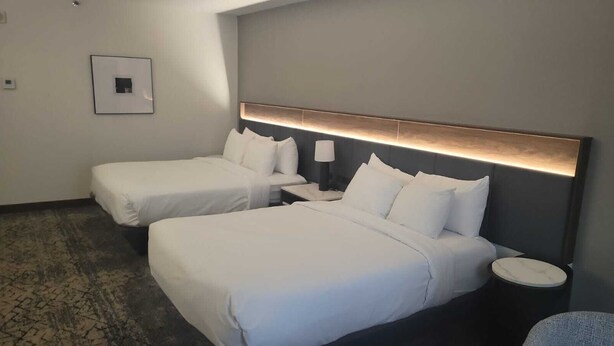 A hotel room with two beds, a nightstand, a lamp, and a small round table. - The Plaza Hotel Columbus at Capitol Square (Columbus)