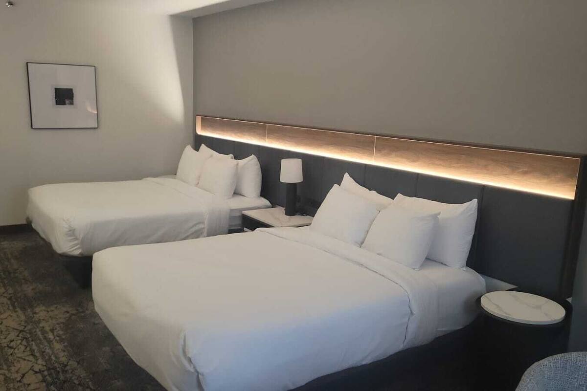 A hotel room with two beds, a nightstand, a lamp, and a small round table.