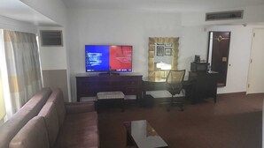 A living room with a flat-screen TV, a sofa, a coffee table, and a dining area with a chair and a lamp. - The Plaza Hotel Columbus at Capitol Square (Columbus)
