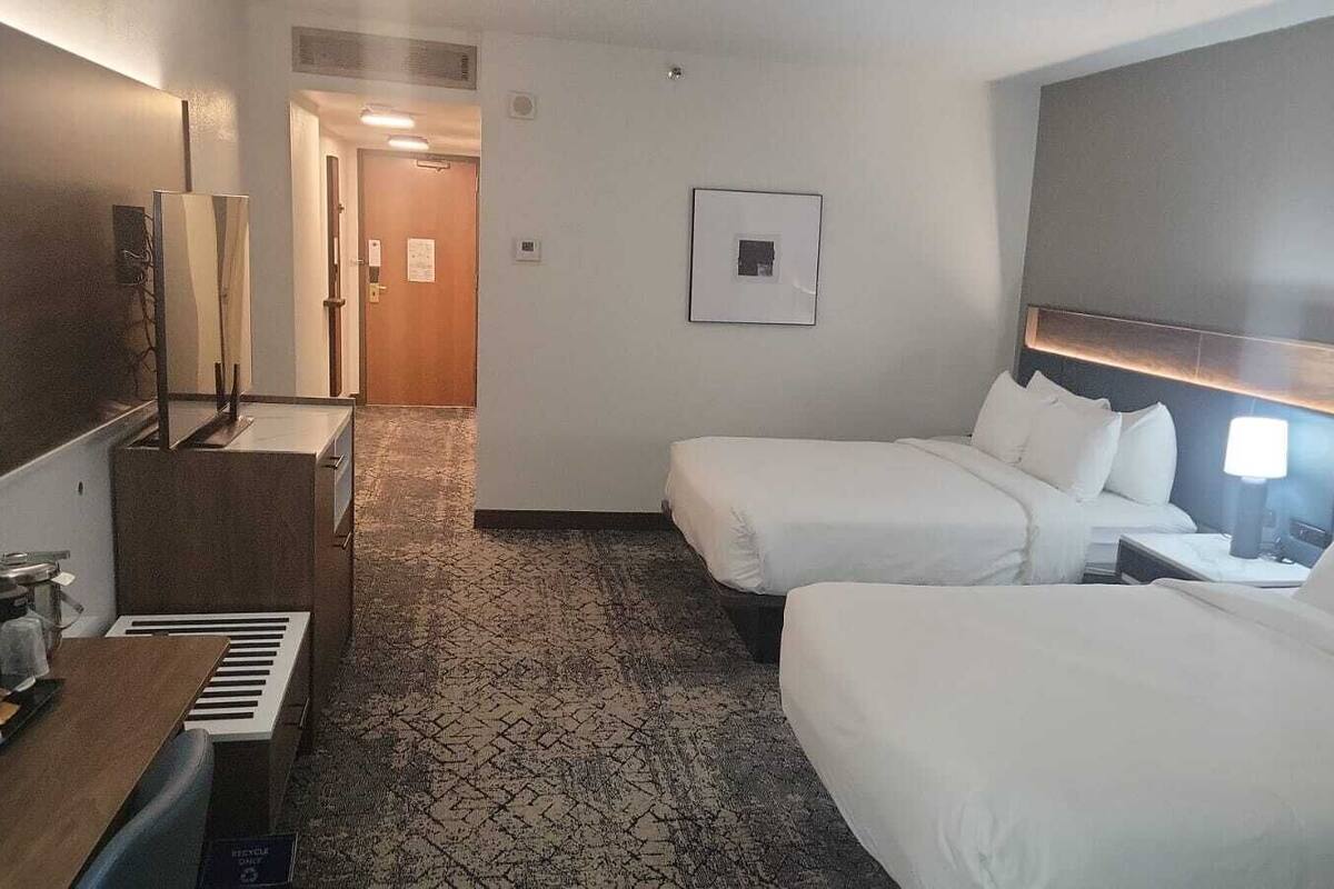 A hotel room with two beds, a desk with a coffee machine, a TV, and a framed picture on the wall.