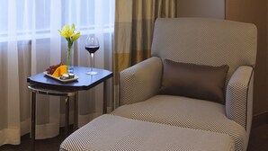 A hotel room with a large armchair, a small table with a plate of fruit and a glass of wine, and a vase with flowers. - The Plaza Hotel Columbus at Capitol Square (Columbus)