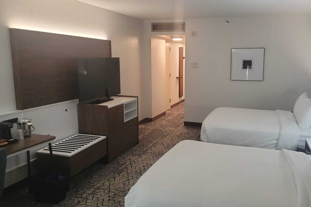Une chambre d’hôtel avec deux lits, un bureau avec un ordinateur, une télévision et une petite kitchenette.