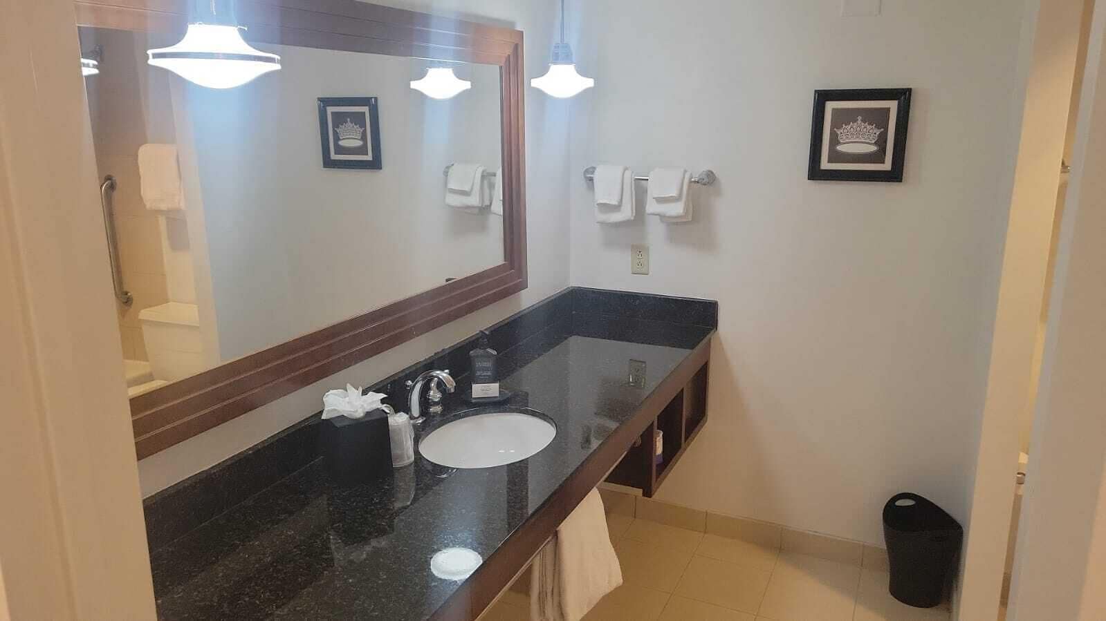 Un baño con un espejo grande, una encimera negra, un lavabo blanco y dos cuadros en la pared.
