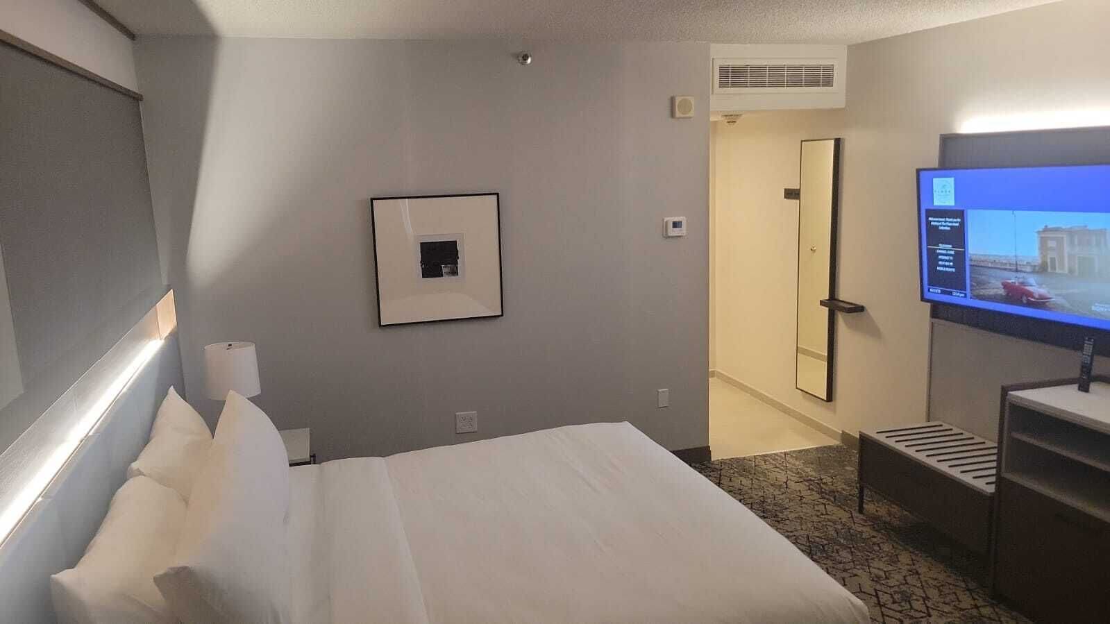 A hotel room with a bed, a television, a framed picture on the wall, and a door leading to another room.