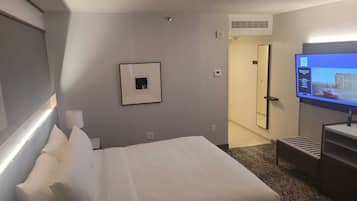 Une chambre d’hôtel avec un lit, une télévision, un tableau encadré au mur et une porte donnant sur une autre pièce.