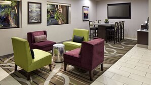 A hotel lobby with green and purple armchairs, a round coffee table, a dining area with a table and chairs, and a flat-screen TV mounted on the wall. - Mission View Inn & Suites San Diego Sea World - Zoo (San Diego)