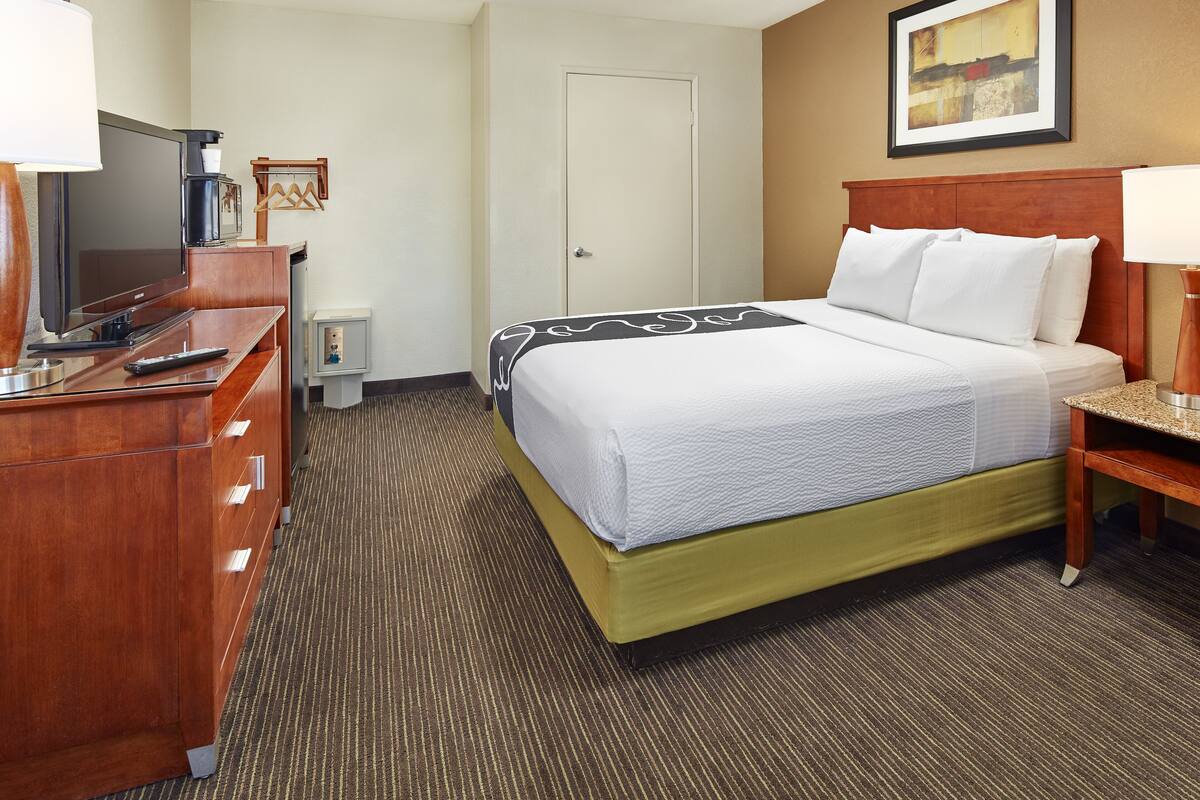 A hotel room with a bed, a TV, a desk, and a door.