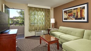 A hotel room with a green sofa, a wooden desk, a lamp, and a painting on the wall. - Mission View Inn & Suites San Diego Sea World - Zoo (San Diego)